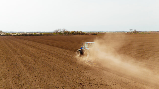 Aerial view of a lone blue tractor churning up the rich, brown soil, kicking up dust under a muted sky in the fields, Sremska Mitrovica, Vojvodina, Serbia.