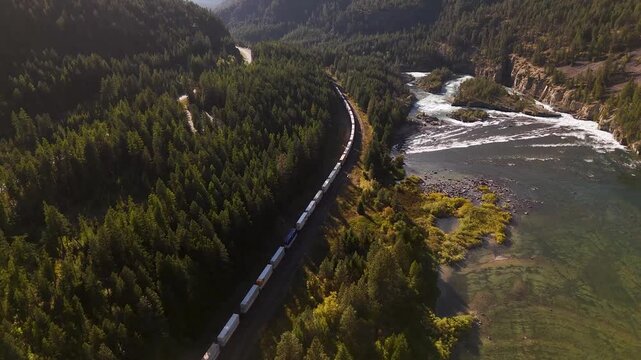 Cinematic aerial view of a long freight train winding through the Canadian Rockies alongside a pristine river valley. Road trip in Canada. Rocky mountains. 4k footage