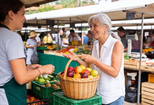Senior woman buying fresh fruit at an outdoor farmers market, friendly conversation with vendor and healthy local food shopping for seasonal produce