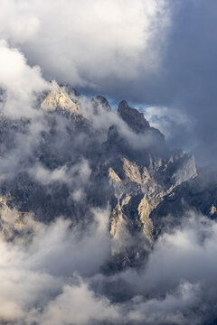 View of rugged mountain peaks piercing through a sea of swirling clouds, bathed in soft light, a symphony of textures, Picos de Europa, Asturias, Spain.
