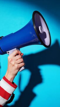Powerful Announcement with a Hand Holding a Blue Megaphone Against a Bright Blue Background for Marketing Campaigns. Vertical. Video. Portrait Orientation.