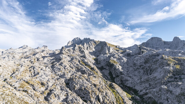 Aerial view of jagged rocky peaks under a serene sky, the rough stone contrasting with the soft clouds, Picos de Europa, Asturias, Spain.