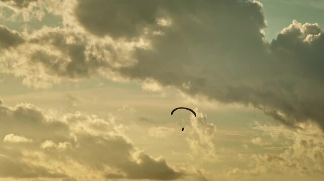 Paraglider soaring high in evening sky, celebrating adventure and freedom against backdrop of golden clouds and sunset setting sun. Active sports outdoors, adventure, recreation in nature landscape