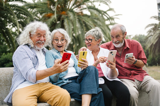 Group of modern senior friends using smartphone app, laughing having fun sharing content on social media