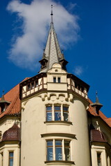 Obraz premium Historic European Tower With Steep Spire and Ornate Turret Under Blue Sky