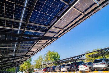 Naklejka premium Engineer in safety vest and helmet pointing towards a solar powered carport, illustrating eco-friendly innovation in parking infrastructure. Solar panels provide shade and sustainable energy.