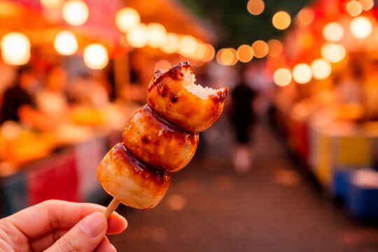 Hand holding a bitten mitarashi dango skewer at a Japanese night festival