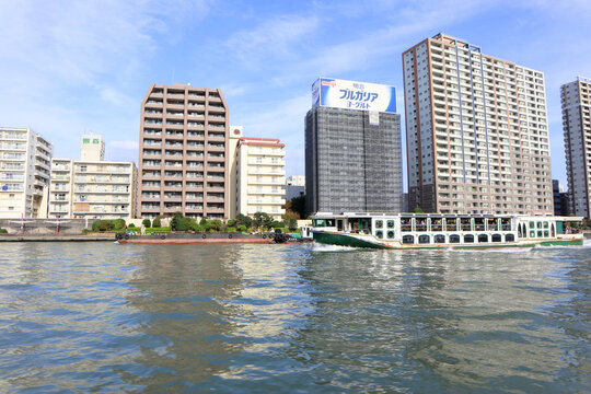Sumida River sightseeing boat cruise passing by modern residential apartment buildings and large corporate advertising billboards in the Tokyo waterfront district - Tokyo, Japan, October 10, 2018