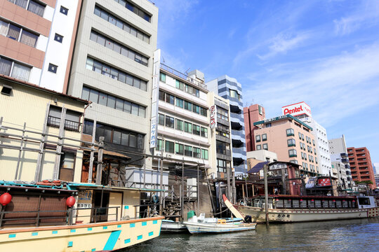 Traditional Yakatabune pleasure boats moored along the Sumida River waterway with modern office buildings and Pentel sign in Shitamachi neighborhood - Tokyo, Japan, October 10, 2018