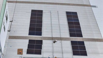 Obraz premium technician in safety gear inspects solar panels on a metal rooftop, holding a tool. The scene emphasizes renewable energy, solar technology, and maintenance of sustainable infrastructure.