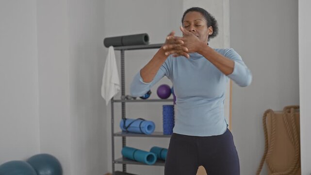 Woman stretches hands forward with fingers interlaced beside foam roller and rolled yoga mat in studio; balance calm wellness.