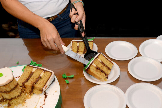 Hands serving layered cake slices on disposable plates at celebration table, casual food sharing moment