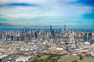 Naklejka premium A wide aerial view shows the dense urban landscape of Queens in the foreground with the iconic Midtown Manhattan skyline across the East River in New York City.