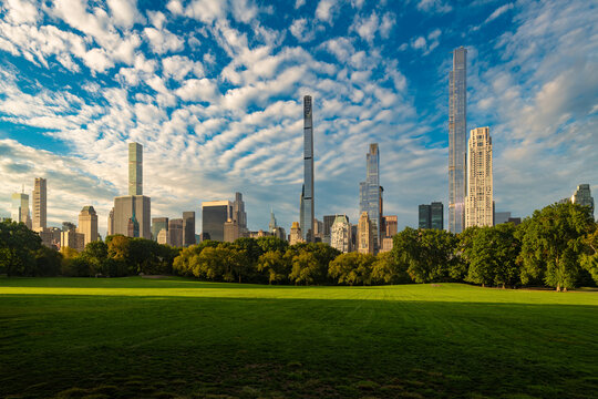 Lush green grass and trees provide a natural foreground to the skyline of Midtown Manhattan from Central Park with the tall and thin ultra luxury skyscrapers of Billionaires Row in New York City.