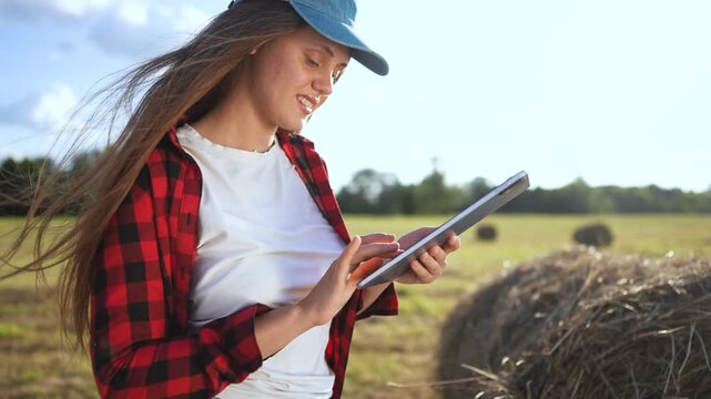 Woman in field holding tablet computer. Girl works on tablet in field. Woman works in a field with haystacks of grass. A woman in lifestyle a field is holding a tablet.