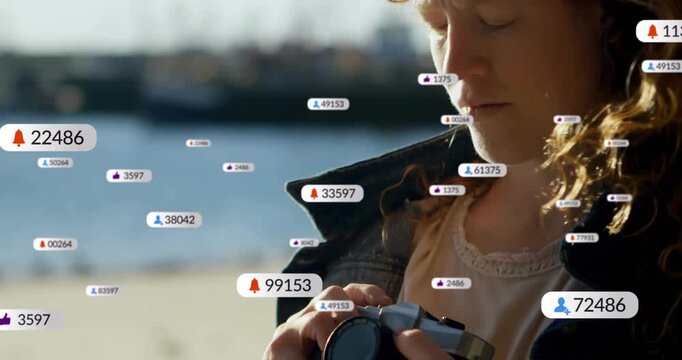 Woman reacting to badges appearing, raising vintage camera to eye, framing pier shot for content