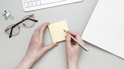 At tidy workspace, woman jots notes on sticky pad surrounded by notebook and stationery supplies © matucha12