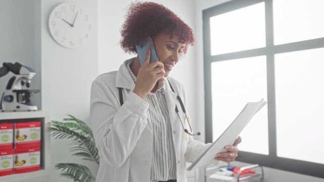 Woman doctor with stethoscope holds phone to ear and reads patient chart in clinic building; focused care.