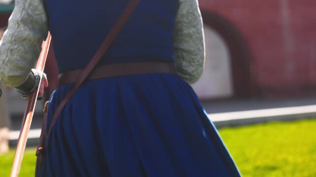 Medieval archery tournament in a castle yard with a woman shooting an arrow from a wooden bow in slow motion. Female archer in traditional medieval dress during historical reenactment, outdoor scene w