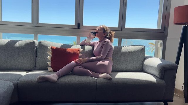 Mujer relajada en el sof&aacute; tomando prote&iacute;na y mirando el mar