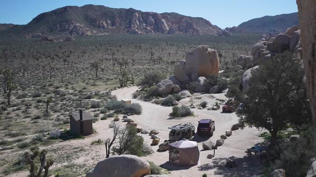 Explore the view of a teardrop camper trailer at a campsite in Joshua Tree National Park surrounded by rocks and desert.