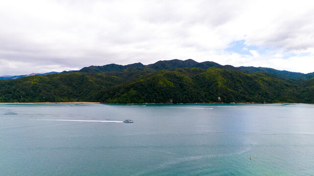 Aerial view of a water taxi slicing through the turquoise waters near the lush, green hills of Abel Tasman National Park, Tasman Region, New Zealand.