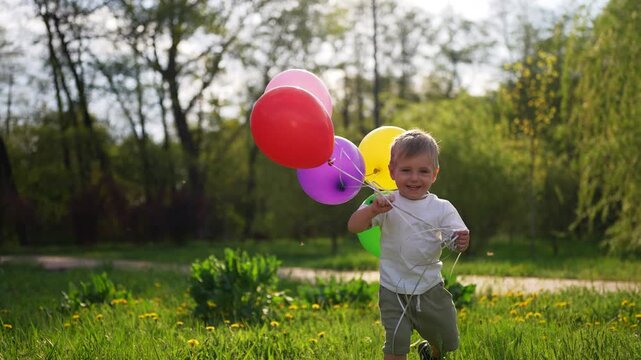 Young boy holding bunch of balloons. Child holding balloons in the summer. A child holding balloons on a grass. A young child grasping lifestyle a cluster of balloons.