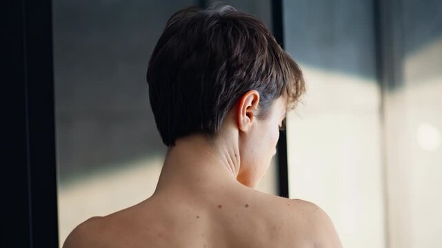 Short haired brunette removing robe closeup. Bare shoulders woman spa session