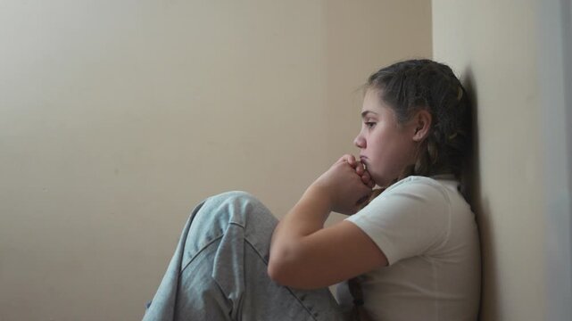 Young girl sitting on the floor. Sad child sits on a corner and is punished. A teenage girl is traumatized by a violent incident. A little girl sitting lifestyle on the ground.