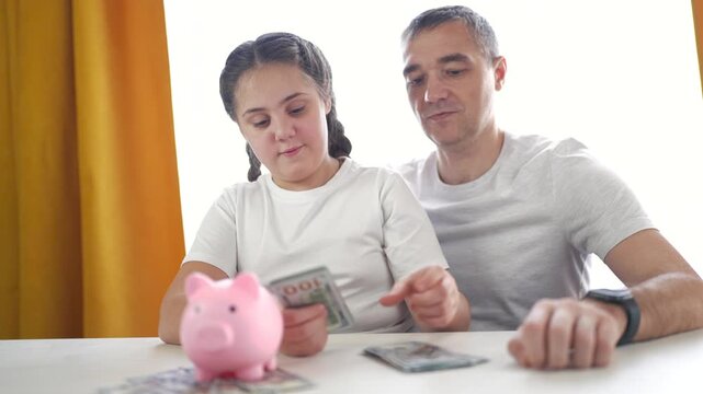 Man and little girl sitting at table with piggy bank. Family counts money in bank. Young girl counts her sons savings. A man and a young girl are seated at a table with a piggy lifestyle bank.