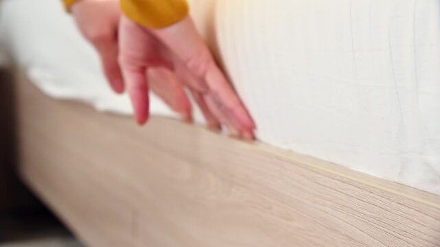 Hand tucking bed sheet under mattress edge in cozy bedroom setting