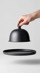 Hand lifting black serving cloche over tray against white background