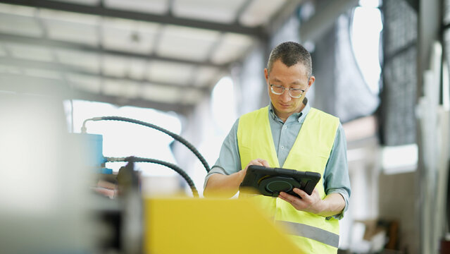 Factory worker wearing reflective vest operating a tablet computer in industrial workshop
