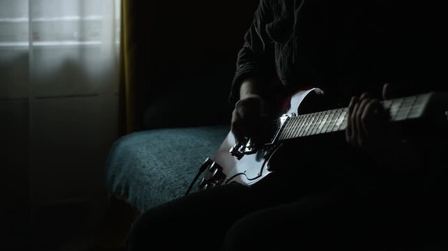 unrecognizable man in black denim playing electric red sg guitar in the day at home. low key light