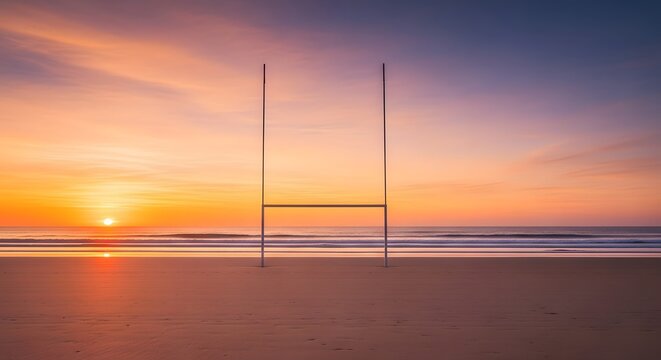 A rugby goal post on a beach at sunset