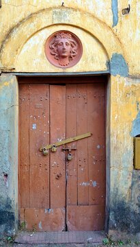 a vertical, close-up shot of a rustic, weathered wooden double door set into a pale yellow and blue stucco wall, characteristic of traditional goa portuguese architecture in areas like panaji or old g