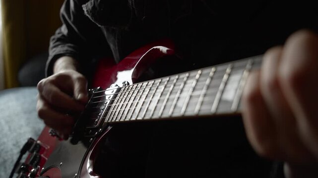 unrecognizable man in black denim playing electric red sg guitar in day at home