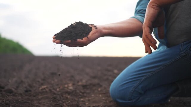 agriculture. man hand holding soil, with particles falling through fingers, set against a blurred outdoor background.. a farmer hand examines the soil agriculture concept