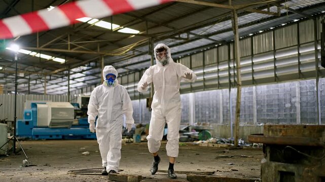 Hazmat suit protective suit protective clothing cleanup crew worker biohazard decontamination industrial warehouse with safety tape during contamination inspection, two technicians respirator suits