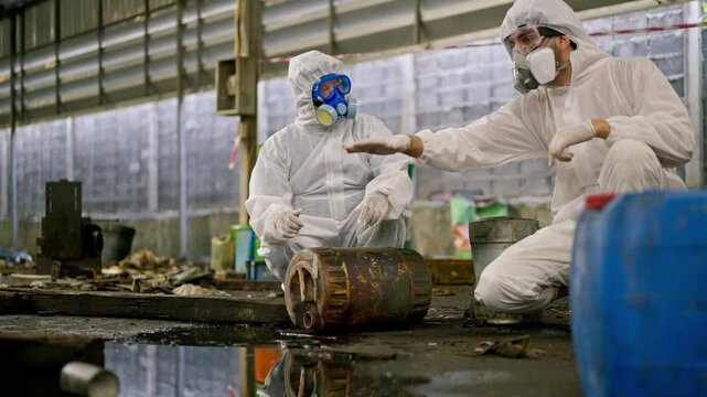 Hazardous waste chemical spill industrial site, hazmat worker protective suit respirator, contamination cleanup operation, toxic pollution control as workers inspect equipment and handle industrial