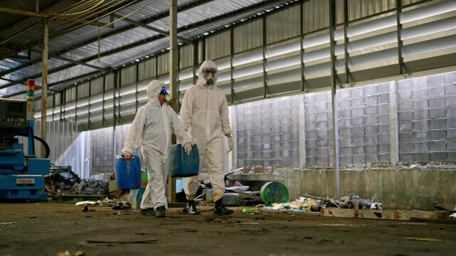 Hazmat suit protective clothing respirator chemical container waste management industrial building hazardous waste industrial factory contamination cleanup, two workers carry container through