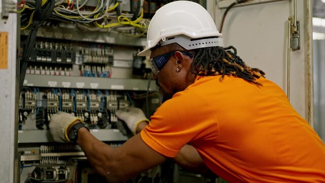 Electrician technician in hard hat performing electrical panel maintenance and wiring for safety in industry, repair work on industrial control cabinet by electrical technician
