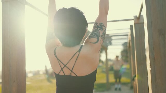 Tattooed athletic woman doing pull-ups outdoor