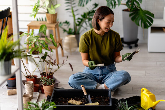 Young woman sitting on the floor planting seeds and reading seed packets, focused and calm while preparing soil indoors&mdash;peaceful home gardening and mindful hobby moment