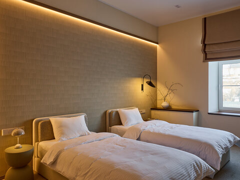 Modern hotel room interior with twin beds, white linens, and a long upholstered headboard. Wooden log side table, lamps, and beige curtains. Minimalist design.