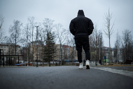 Hooded Man Walking Away in Overcast Urban Park