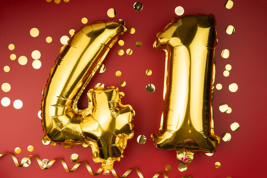 41st birthday celebration. Gold festive balloons number 41 year anniversary on red background with confetti. Birthday or wedding event.