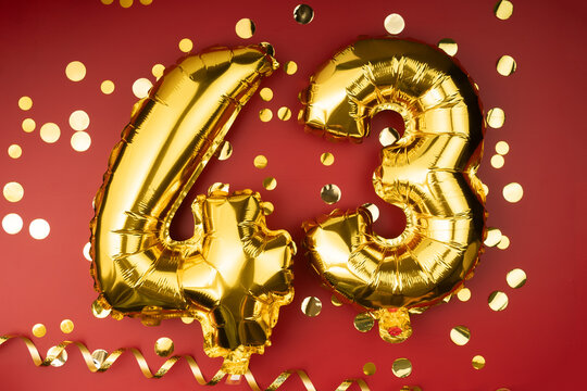 43rd birthday celebration. Gold festive balloons number 43 year anniversary on red background with confetti. Birthday or wedding event.
