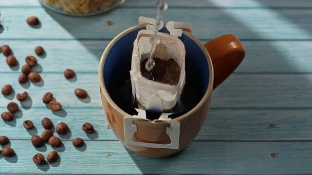 A coffee drip bag being filled with water in a mug, surrounded by coffee beans. Concept of coffee making, morning routine, and specialty brewing techniques, cafe and restaurant advertisements.