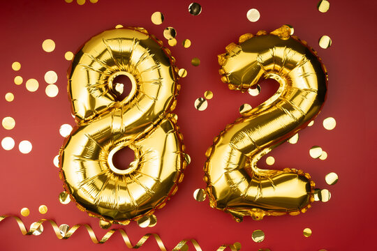 82nd birthday celebration. Gold festive balloons number 82 year anniversary on red background with confetti. Birthday or wedding event.